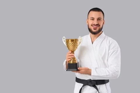 Young man with gold cup practicing karate on light background Stock Photos