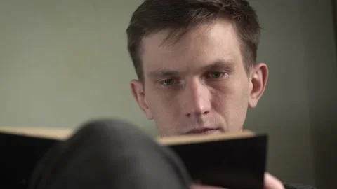 Young man in gray sweater reading a book sitting in an armchair at home. Stock Footage 235529477