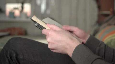 Young man in gray sweater reading a book sitting in an armchair at home. Stock Footage 235615527