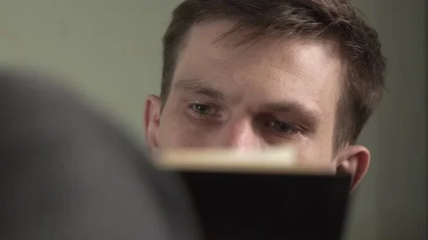 Young man in gray sweater reading a book sitting in an armchair at home. Stock Footage 235615529