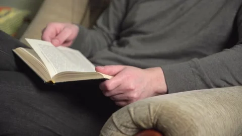 Young man in gray sweater reading a book sitting in an armchair at home. Stock Footage 235615665