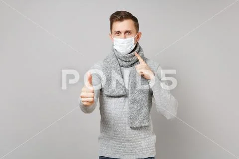 Young man in gray sweater, scarf pointing index finger on sterile face mask Stock Photos