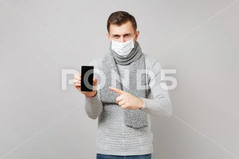 Young man in gray sweater, scarf sterile face mask pointing index finger on Stock Photos