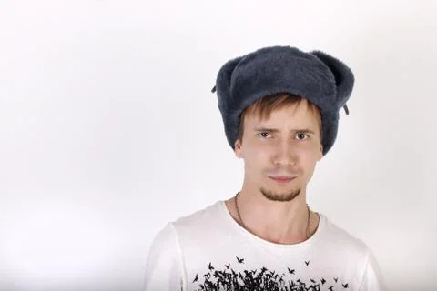 Young man in grey cap with earflaps looks surprised in studio Stock Photos