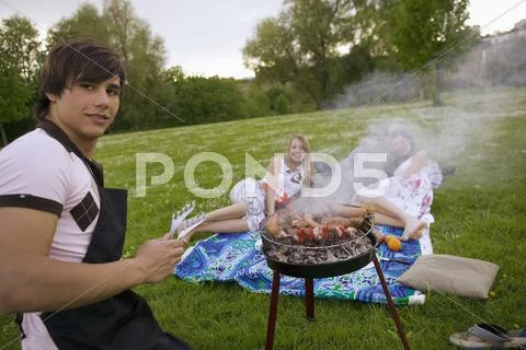 Young man grilling young women in background Stock Photos