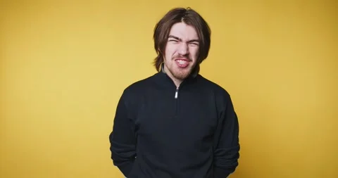 Young man grimaces playfully on yellow background, showing a humorous expre.. Stock Footage 314337025