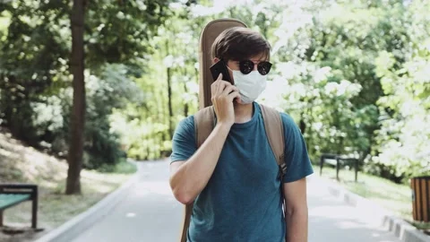 Young man with a guitar on the back is walking in the park and talking on phone. Stock Footage 141448328