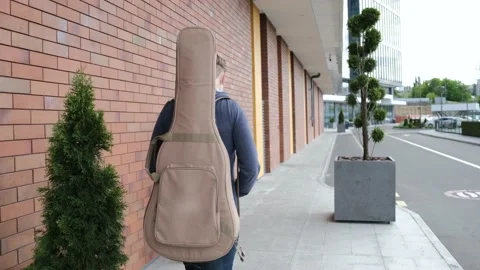 A young man with guitar in the back is walking alone, back view. Stock Footage 141448840