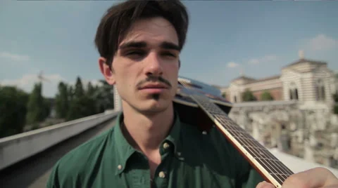 A young man with a guitar walking down the street, steadicam shot Stock Footage 60240256