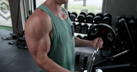 Young man in the gym doing biceps exercise lifting a barbell 動画素材 158916552