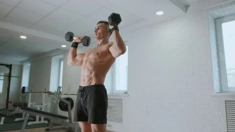 Young man in gym performs squats and raises his arms up with dumbbells. Working Vidéo 271246436
