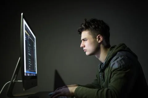 Young man hacking server in dark room. Young man programm code on pc in dark  库存照片