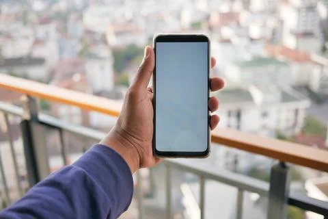 Young man hand using smart phone with green screen against city buildings Stock Photos