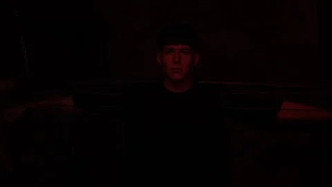 A young man is handcuffed to a wall in a dark room with a flashing red light. Stock Footage 311796778