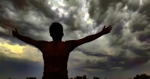 A young man hands up and looking at thunderstorm cloudscape, praying to god Stock Photos