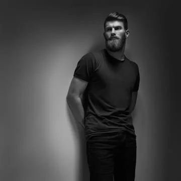 Young man with hands in pockets leaning against grey studio wall Stock Photos