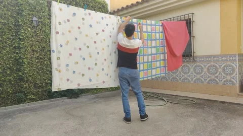 Young man hanging wet laundry to dry outside Vídeo Stock 344692426