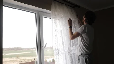 A young man hangs curtains on the window Stock Footage 129341244