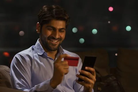 A YOUNG MAN HAPPILY USING DEBIT CARD TO MAKE ONLINE PAYMENTS Stock Photos