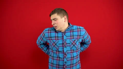 A young man has a backache and is holding it in his hands. Shooting on a red Stock Footage 147394386