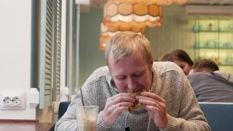 Young man has lunch in a cafe with a sandwich. blonde with a beard eating a Stock-Footage 142224534