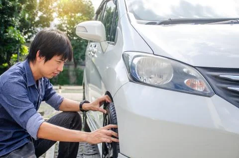Young man has problems with the wheel of his car. He is kneeing and Check Foto stock