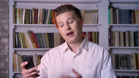 Young man has video call on smartphone in library, communication concept Video stock 92302851