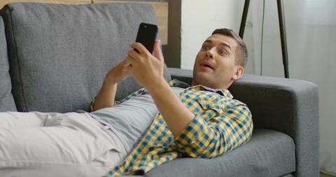 Young man has a video chat on smartphone, lying on sofa Stock Footage 114881713