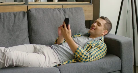 Young man has a video chat, lying on sofa at home Stock Footage 114882701