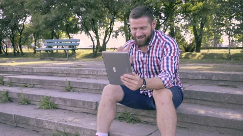 Young man has video conversation by tablet, sitting on stairs. Video stock 67242528