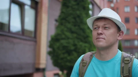 Young man in hat and backpack walks around the city, camera tracking Stock Footage 145412334