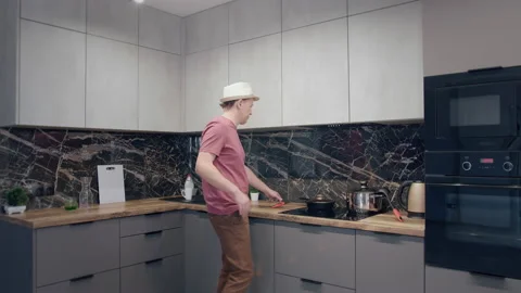 Young man in a hat dancing and singing in the kitchen while cooking Stock Footage 167146640