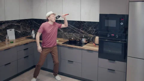 Young man in a hat dancing in the kitchen, singing in the scoop cooking, good Stock Footage 163776775