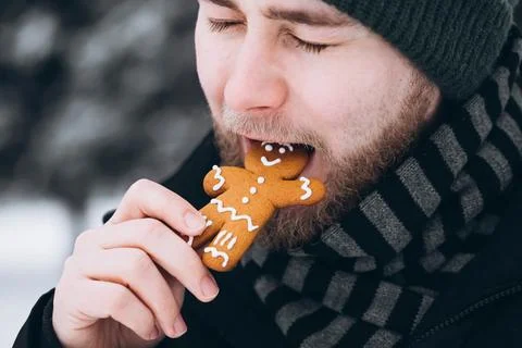 A young man in a hat eats a gingerbread man, close-up. Foto stock