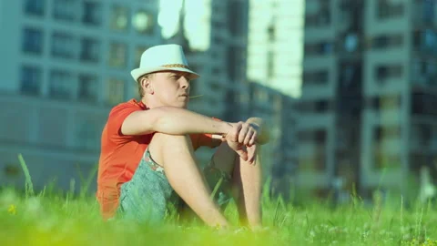 Young man in hat is resting while sitting on the grass in a city park, tracking Stock Footage 143491210