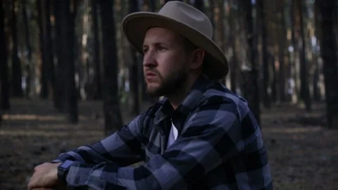 Young man with hat resting while hiking in the mountains or forest at sunset. Stock Footage 150255965