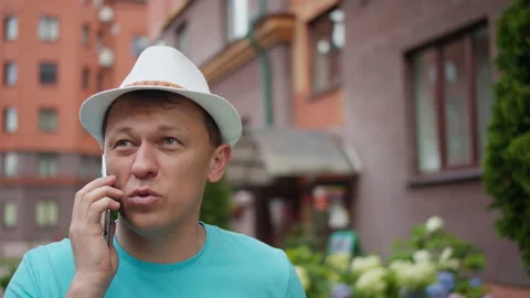 Young man in hat talking on mobile phone in the street, camera tracking Stock Footage 139916733