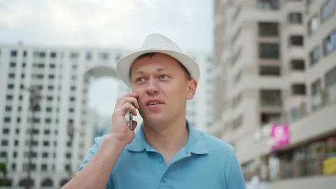 Young man in hat talking on a mobile phone while standing on a city street Stock Footage 143343586