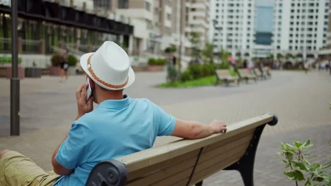 Young man in a hat talking on the phone while sitting on a bench, camera Stock Footage 140676912