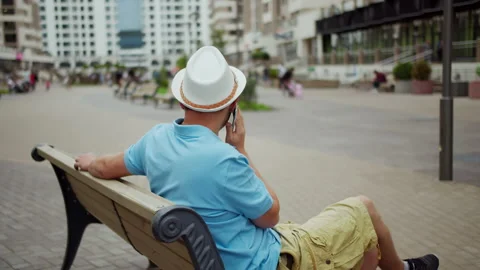 Young man in hat talking on the phone while sitting on a bench, camera movement Stock Footage 141366745