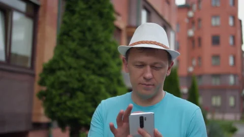 Young man in hat texting on the phone, walking down the street, tracking camera Stock Footage 137534892