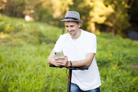 Young man in hat use mobile phone, book online rental electric scooter Foto stock