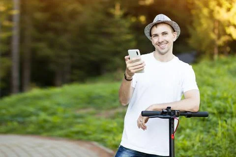 Young man in hat use mobile phone, book online rental electric scooter Stock Photos