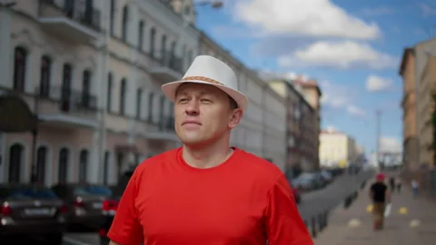 Young man in a hat walks along the city street, puts on sunglasses Stock Footage 135761645