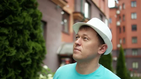 Young man in a hat walks along the city street watches around, camera tracking Stock Footage 150803483