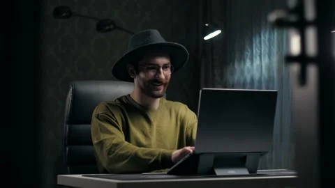 Young man with a hat work remotely sitting at the desk.Attractive guy using Stock Footage 232132191