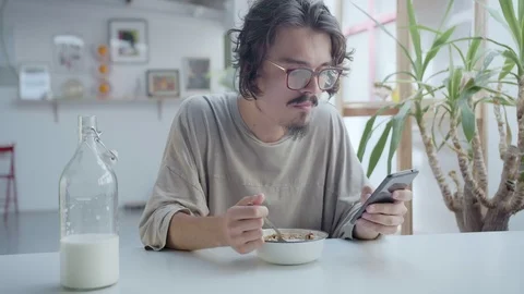 Young man having breakfast and chatting by mobile app or social by smartphone Stock Footage 98895374