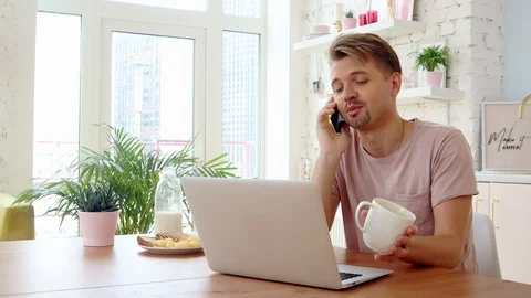 Young man having breakfast in his kitchen and using his laptop and smartphone. Stock Footage 119137472
