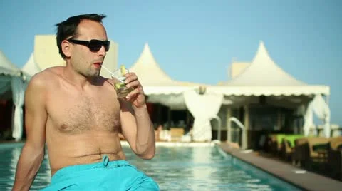 Young man having a drink by the pool HD Stock Footage 10888349