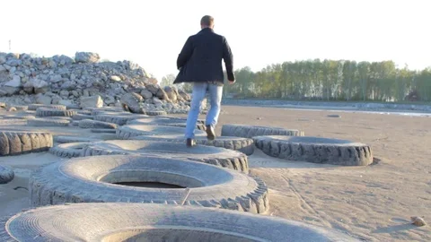 Young man having fun outdoor: running on the big tires at sunny sandy beach Stock Footage 75606319